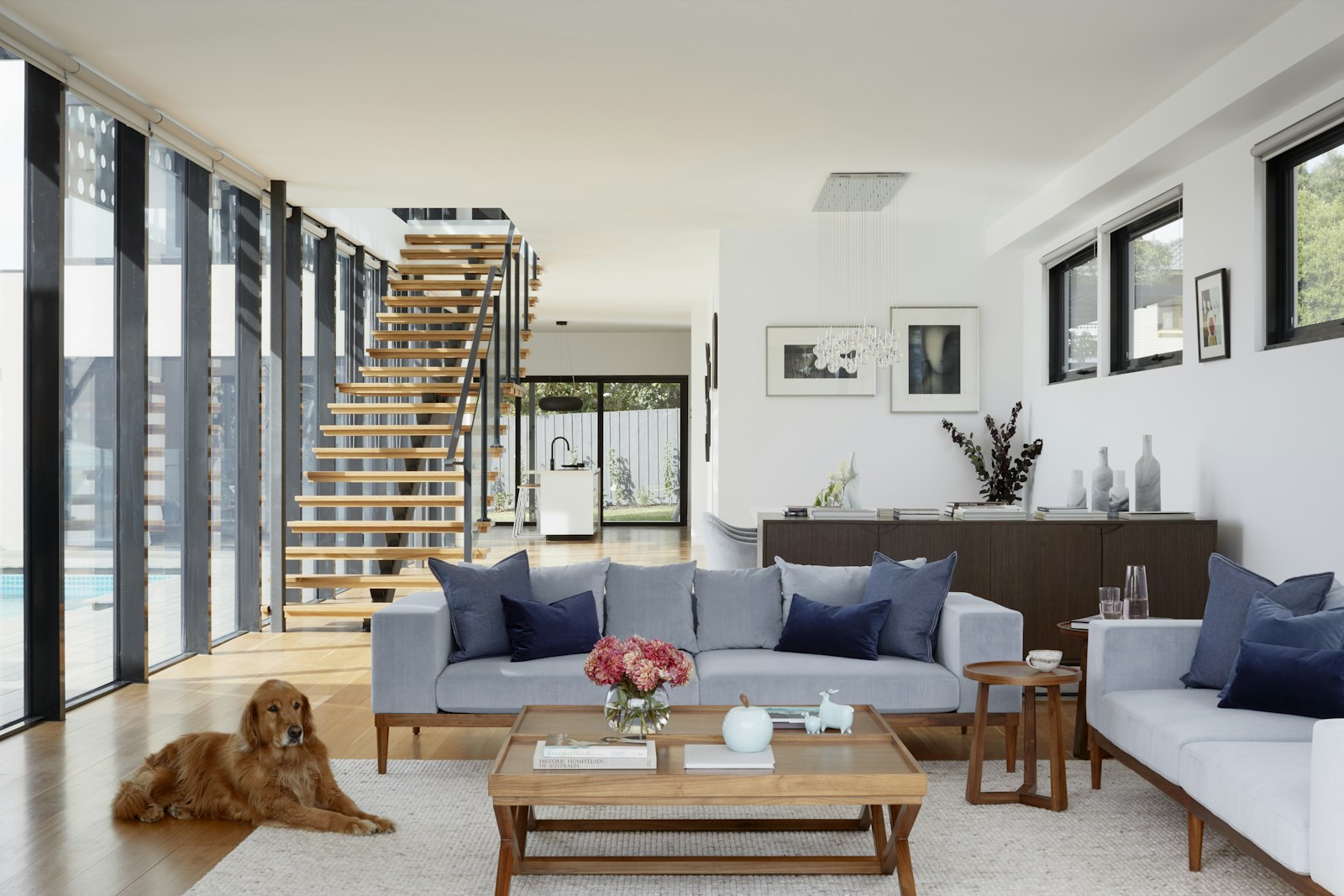 Salón de una vivienda nueva con escalera de madera y sofás claros. Imagen de referencia.